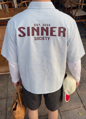 Person wearing a shirt with 'Sinner Society' text in an outdoor setting